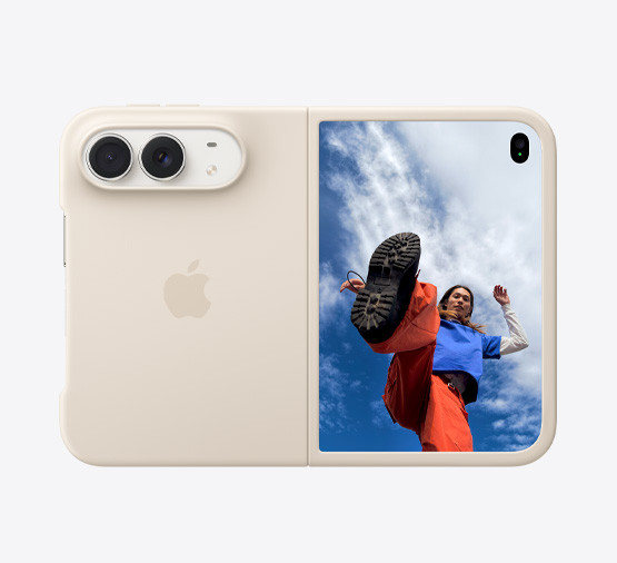 套上沙色矽膠護殼的星光色 iPhone Duo，橫向完全打開，雙融合相機位於左上方，護殼包覆機身背面和正面顯示器的邊緣，右側外螢幕展示有人站在藍天白雲之下的影像